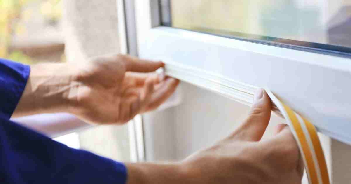 Hands applying weatherproofing seal to a window frame.